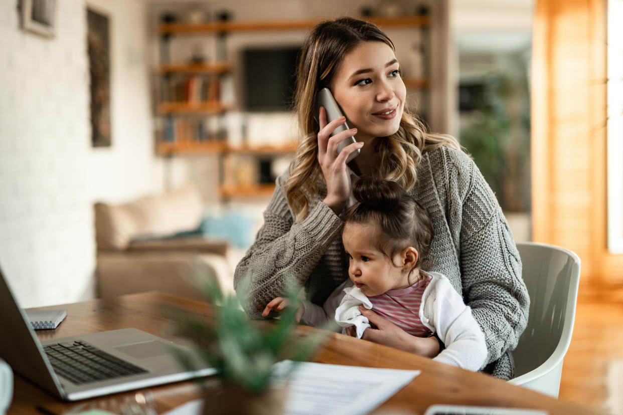 Smiling mother holding small daughter in her lap while talking on the phone at home.