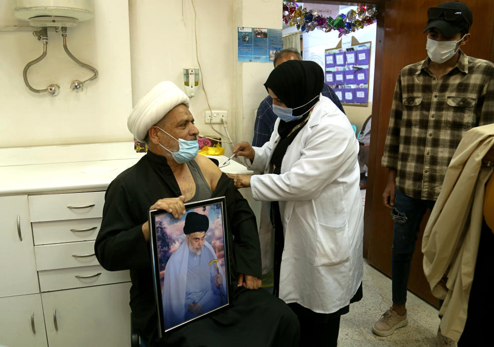 A follower of populist Shiite cleric Muqtada al-Sadr holds a picture of him while receiving a dose of the Chinese Sinopharm coronavirus vaccine at a clinic in Sadr City, Baghdad, Iraq, Wednesday, May 4, 2021. Iraq’s vaccine rollout had been faltering for weeks. Apathy, fear and rumors kept many from getting vaccinated despite a serious surge in coronavirus infections and calls by the government for people to register for shots. It took al-Sadr’s public endorsement of vaccinations — and images of him getting the shot — to turn things around. (AP Photo/Hadi Mizban)