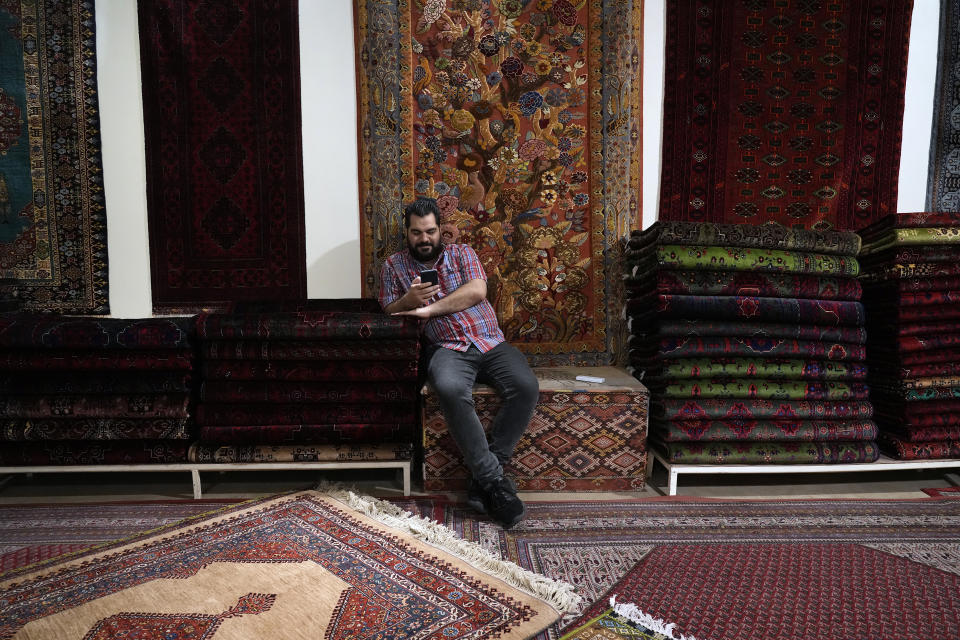 A salesman works on his cell phone at a carpet shop in the old main bazaar of Tehran, Iran, Thursday, June 13, 2024. The rise of the “Hamster Kombat” app in Iran highlights a harsher truth facing the Islamic Republic's economy ahead of its presidential election this week to replace the late President Ebrahim Raisi, who died in a helicopter crash in May. (AP Photo/Vahid Salemi)