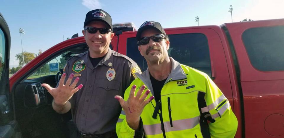 This Friday, Oct. 11, 2019, photo released by the North Davis Fire District shows Chief Allen Hadley, left, and Cpt. Kevin Lloyd In Clearfield, Utah. The two Utah firefighters are receiving praise after they found a creative way to keep a young girl calm at the scene of a car accident. North Davis Fire District Fire Chief Mark Becraft said the firefighters let a young girl paint their nails after she and her mother were in a car accident Saturday. Chief Hadley and Cpt. Lloyd checked on the crying and screaming girl while medics evaluated her mother. Nobody was seriously injured. (Charlotte Coyle/North Davis Fire District via AP)