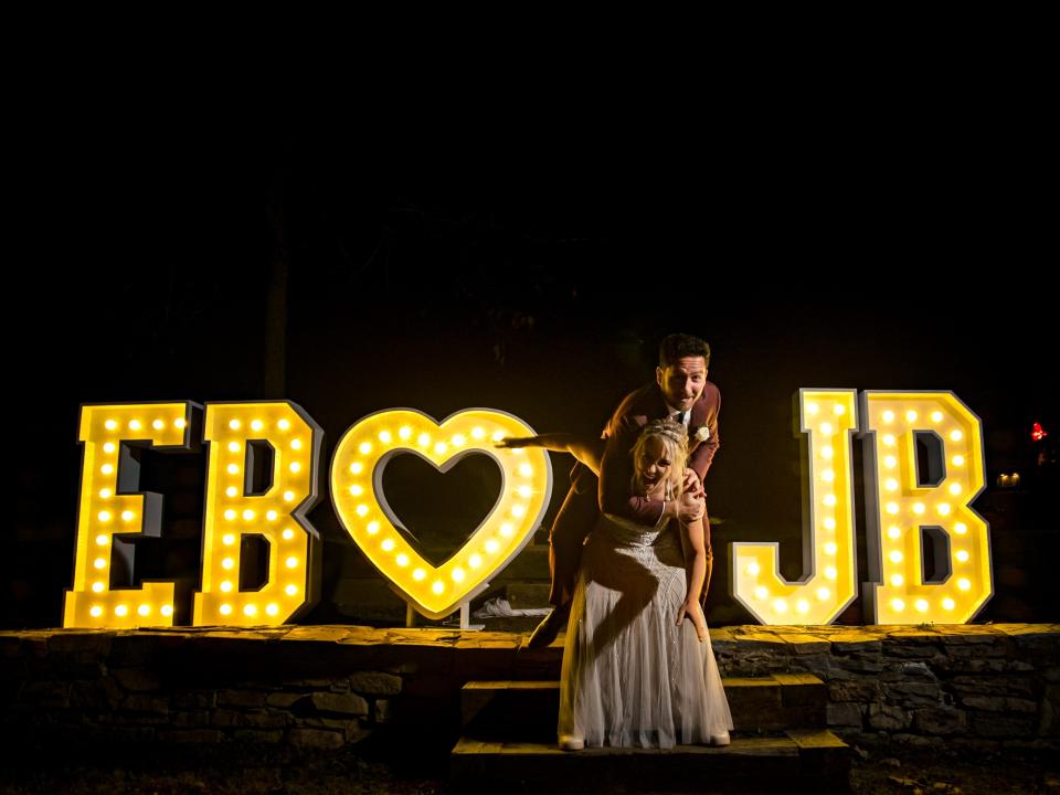 The bride and groom posing in front of light up initials at campground wedding