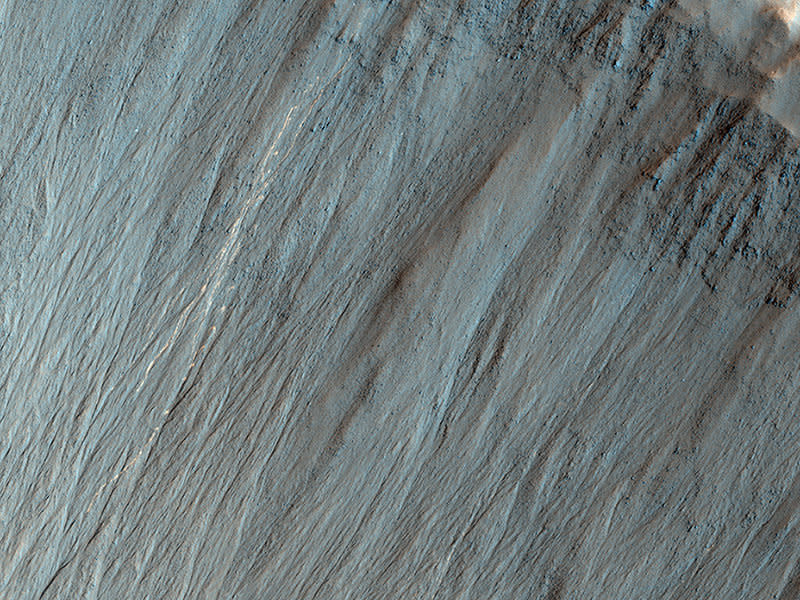 This image shows a well-preserved impact crater. A closeup view highlights distinctive bright lines and spots on the steep slope on the north side.    No such pattern was visible when HiRISE imaged this crater 5 years ago (2.6 Martian years ago), in March 2008. The discontinuous bright spots indicate bouncing, thus these features are interpreted  to be a result of boulders bouncing and rolling down the slope.     Where did the boulders come from? Maybe they fell from the crater's steep upper cliffs, although we don't see any new bright features there that point to the source. Maybe the rocks were ejected from a new impact event somewhere nearby.    Why are the trails bright? Perhaps the shallow subsurface soil here is generally brighter than the surface soil, as revealed by the Spirit rover in a part of Gusev Crater. It can't be bright from ice because this is a warm equator-facing slope seen in the summer.    (Caption: Alfred McEwen)