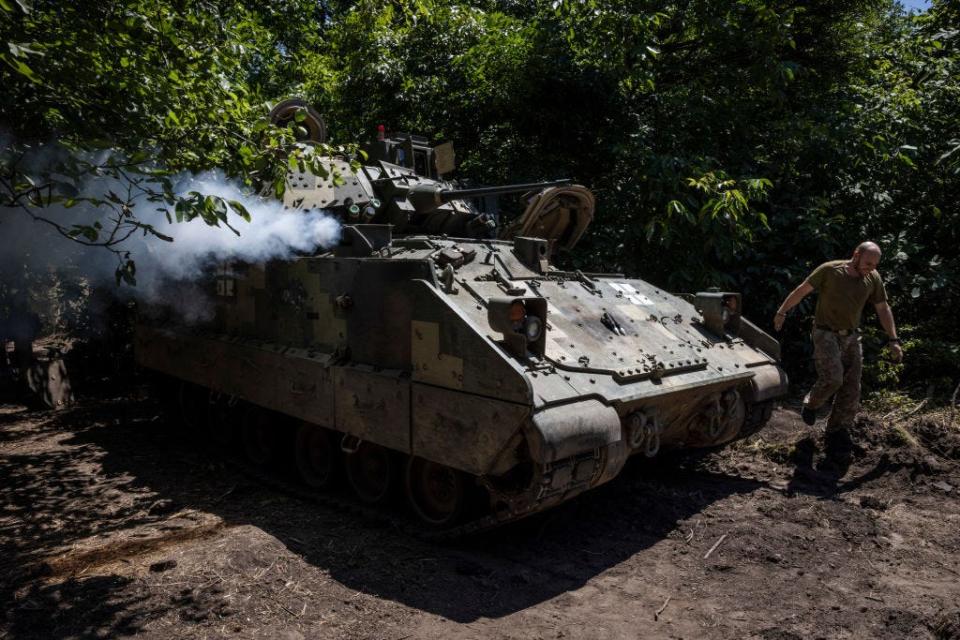 A soldier from Ukraine's 47th Mechanized Brigade runs past a US made Bradley Fighting Vehicle as the engine is started at a secret workshop in a wooded area in Zaporizhzhia Region, Ukraine