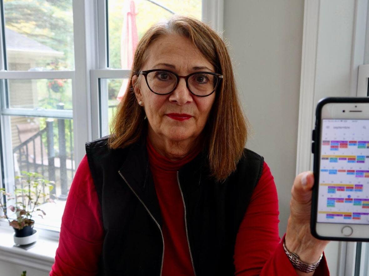 Ginette Perron Davidson, 73, holds up her cell phone which displays her agenda. She says she has colour-coded all of her husband’s medical sessions, appointments with specialists and schedules. She and her husband are among 73,000 in the Eastern Townships without a family doctor.  (Rachel Watts/CBC - image credit)