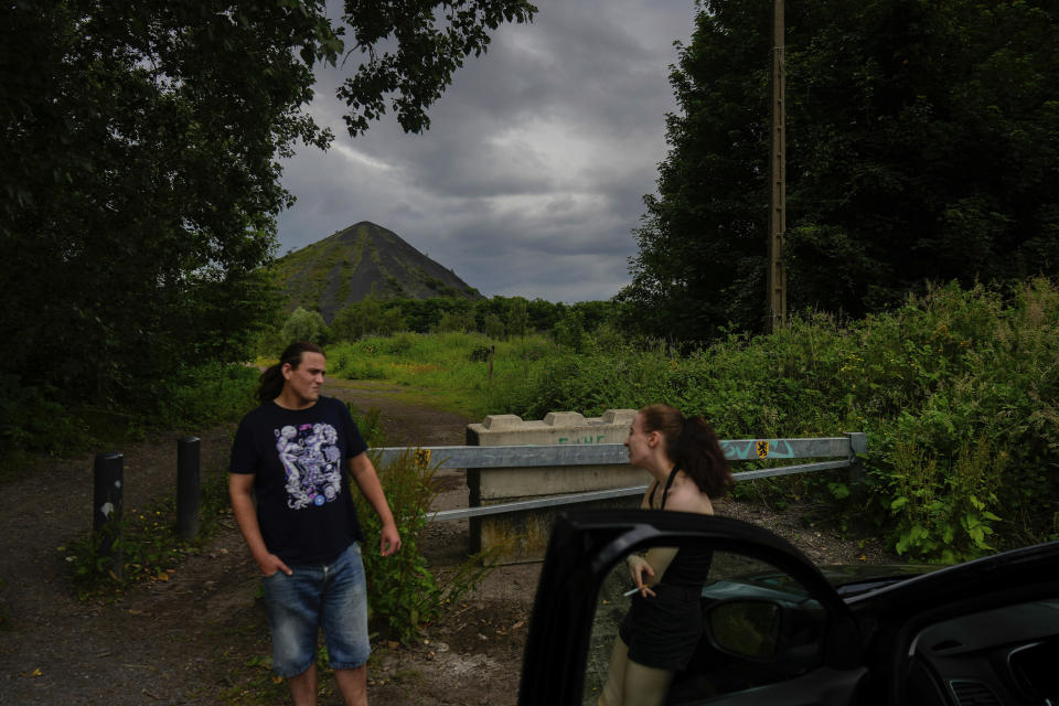 People speak and smoke with the Saint Henriette slag heap, in the background, in Henin-Beaumont, northern France, Sunday, June 30, 2024. Several waves of industrial shutdowns have left unemployment levels above the national average, and 60% of the population earns so little it does not need to pay tax, according to data from France's national statistics agency. (AP Photo/Thibault Camus, File)