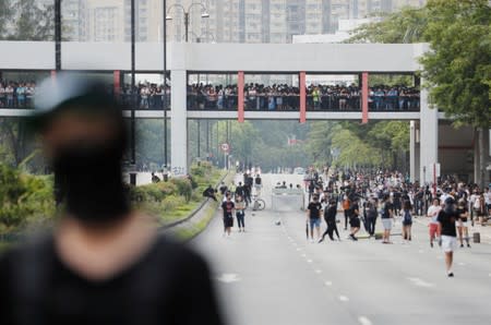 Anti-government protesters walk on the street while people watch from a bridge during a protest in Tai Po district, in Hong Kong