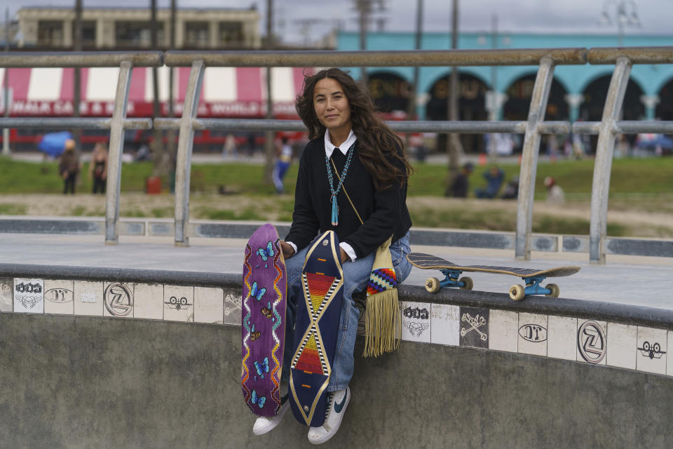 Di'Orr Greenwood, an artist born and raised in the Navajo Nation in Arizona and whose work is featured on the new U.S. stamps, poses for a picture with her skateboards in the Venice Beach neighborhood in Los Angeles Monday, March 20, 2023. On Friday, March 24, the U.S. Postal Service is debuting the "Art of the Skateboard," four stamps that will be the first to pay tribute to skateboarding. The stamps underscore how prevalent skateboarding has become, especially in Indian Country, where the demand for designated skate spots has only grown in recent years. (AP Photo/Damian Dovarganes)