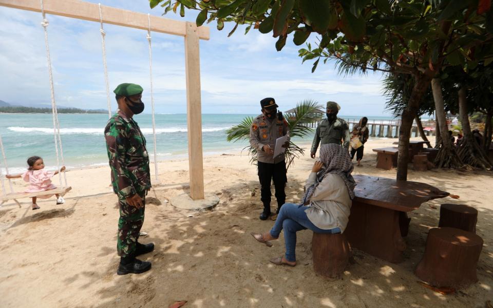 Indonesian officers carry out security checks on people failing to wear protective masks, at a beach in Aceh Besar - Shutterstock 