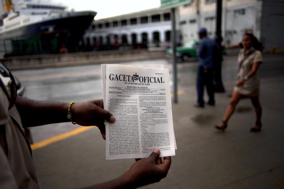 A man holds up a copy of Cuba's Tuesday's official gazette where the new migratory policy that will no longer require islanders to apply for an exit visa is published, in Havana, Cuba, Tuesday, Oct 16, 2012. The Cuban government announced Tuesday that it will eliminate the much-loathed bureaucratic procedure that has been a major impediment for many seeking to travel overseas for more than a half-century. (AP Photo/Ramon Espinosa)