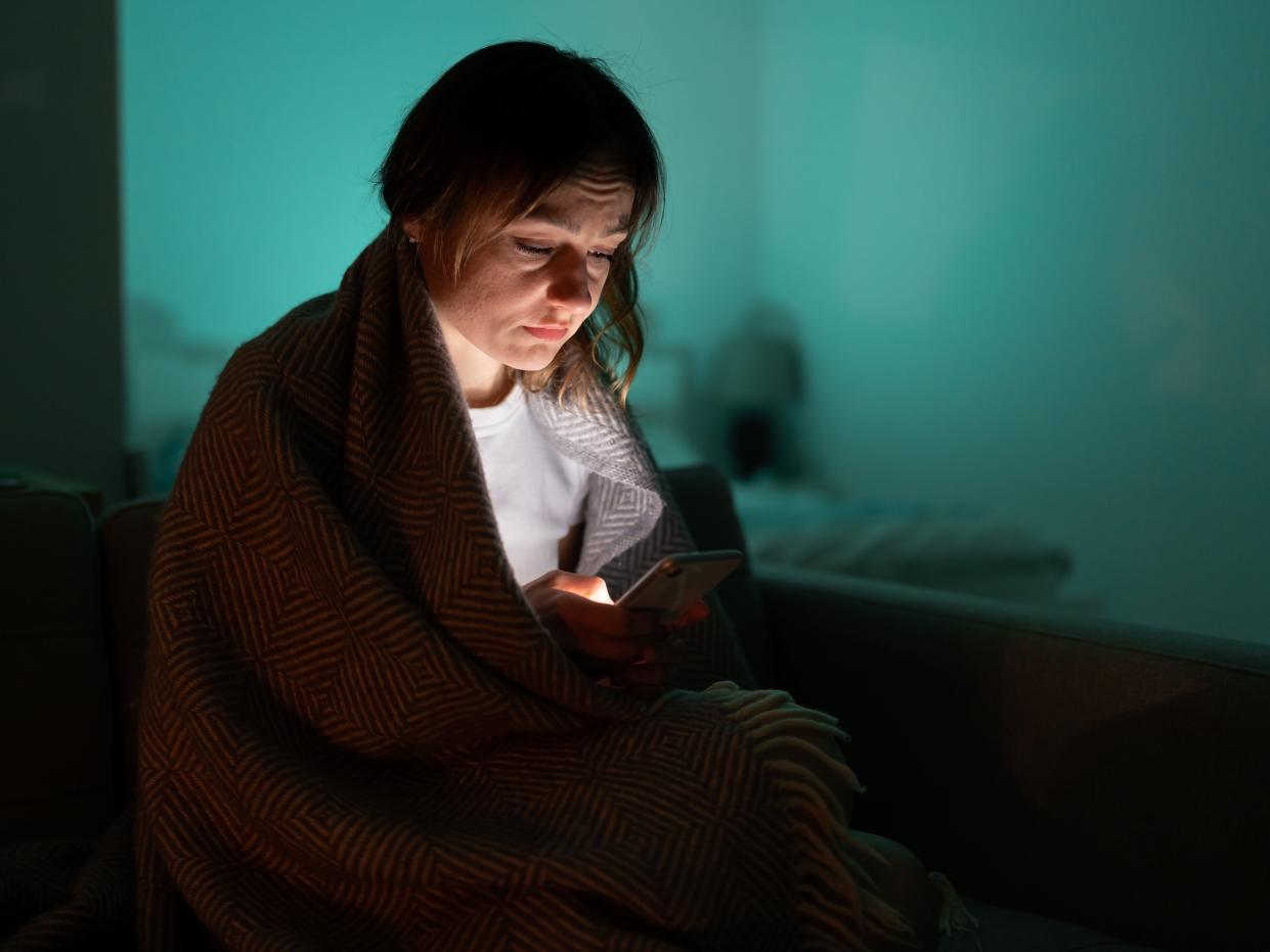 Woman looking at her phone in the dark covered by a blanket.