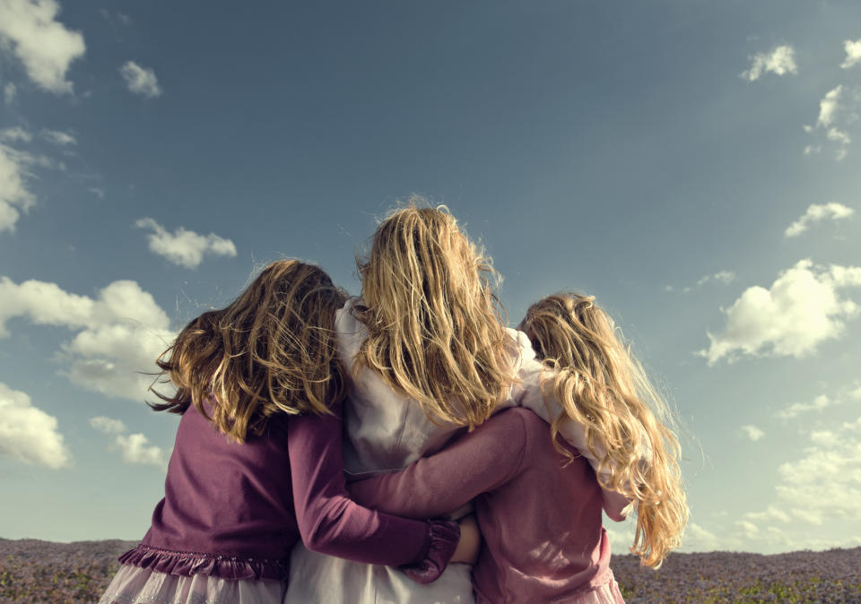 Rear view of three girls in pink looking out over field of purple wildflowers