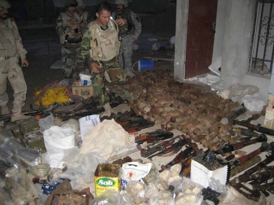 Iraqi forces stand next to a cache of weapons, ammunition, and other items found during a raid alongside US forces in 2007. <em>US Army</em>
