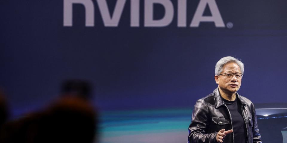 Jensen Huang of Nvidia in a leather jacket and talking onstage with a large Nvidia logo behind him