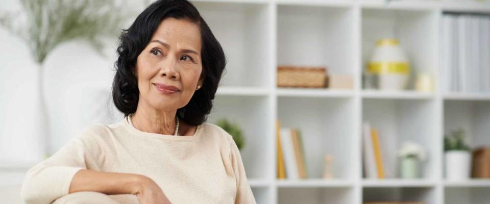 Pensive Vietnamese mature woman sitting on the sofa at home