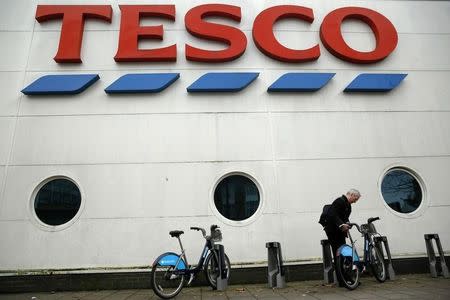 A man unlocks a bicycle outside a branch of Tesco supermarket in London January 5, 2015. REUTERS/Luke MacGregor