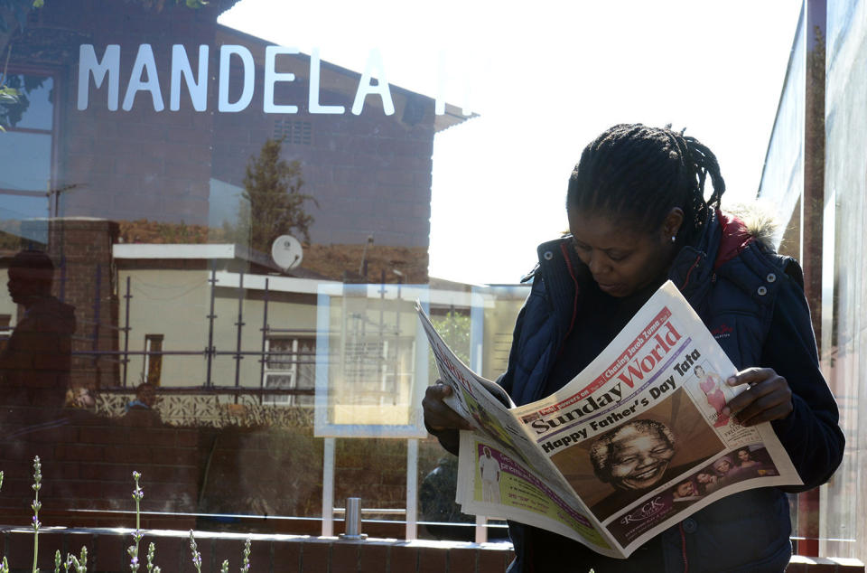 Tour guide Oarabile Monakwane, reads a newspaper wishing former president Nelson Mandela, or 'Tata' as he is affectionately known, a Happy Father's day, outside the home, turned museum, where Mandela lived, in Soweto, South Africa, Sunday, June 16, 2013. South Africa's president says that Nelson Mandela is seeing sustained improvement from the recurring lung infection that is forcing him to spend a ninth day in the hospital. (AP Photo/Lungelo Mbulwana)