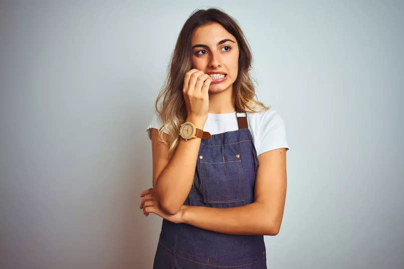 Young beautiful woman wearing apron over grey isolated background looking stressed and nervous with hands on mouth biting nails. Anxiety problem.