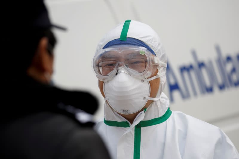 FILE PHOTO: A hospital staff member in protective garments talks to a police officer at a checkpoint to the Hubei province exclusion zone at the Jiujiang Yangtze River Bridge in Jiujiang