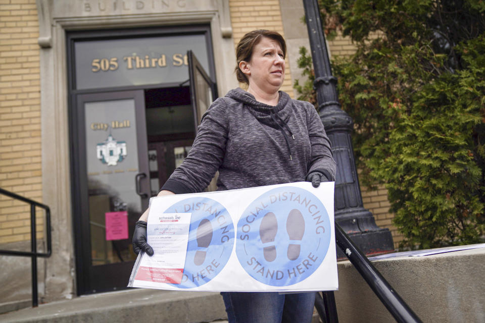 Hudson, Wis., city clerk Becky Eggen displays some of the health alert and social distancing signs Monday, April 6, 2020, that were to be used in Tuesday's election, postponed by the governor Monday afternoon. Wisconsin Gov. Tony Evers on Monday moved to postpone the state's presidential primary for two months because of the coronavirus pandemic, prompting a court challenge and adding to confusion about whether voters will be able to head to the polls on Tuesday. (Glen Stubbe/Star Tribune via AP)