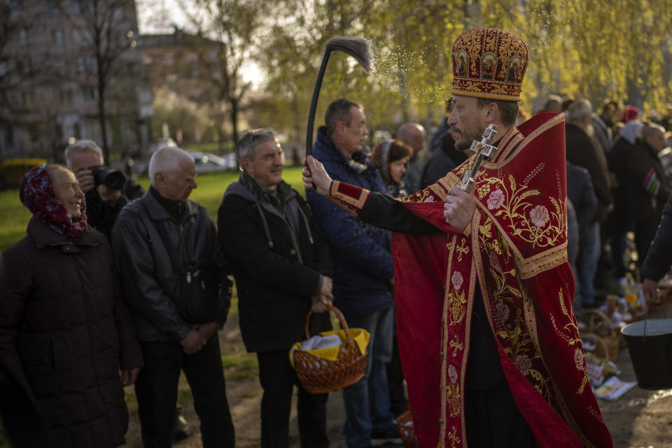 An orthodox Ukrainian priest blesses believers as they collect traditional cakes and painted eggs prepared for an Easter celebration during a religious service at a church in Bucha, on the outskirts of Kyiv, on Sunday, April 24, 2022. (AP Photo/Emilio Morenatti)