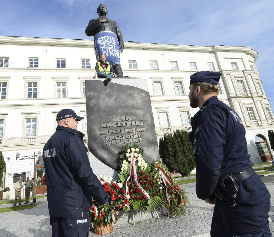 A man sits on a monument to Poland's late president Lech Kaczynski in downtown Warsaw, Poland, Friday, Oct. 11, 2019. He wrapped it in a banner reading 'Where is the Wreckage?' of the plane that crashed in 2010 in Russia, killing the president. Just two days ahead of parliamentary elections, this is criticism of the ruling Law and Justice party, led by the late president's twin Jaroslaw Kaczynski, which has vowed to bring the wreckage back from Russia, where it remains. (AP Photo/Czarek Sokolowski)