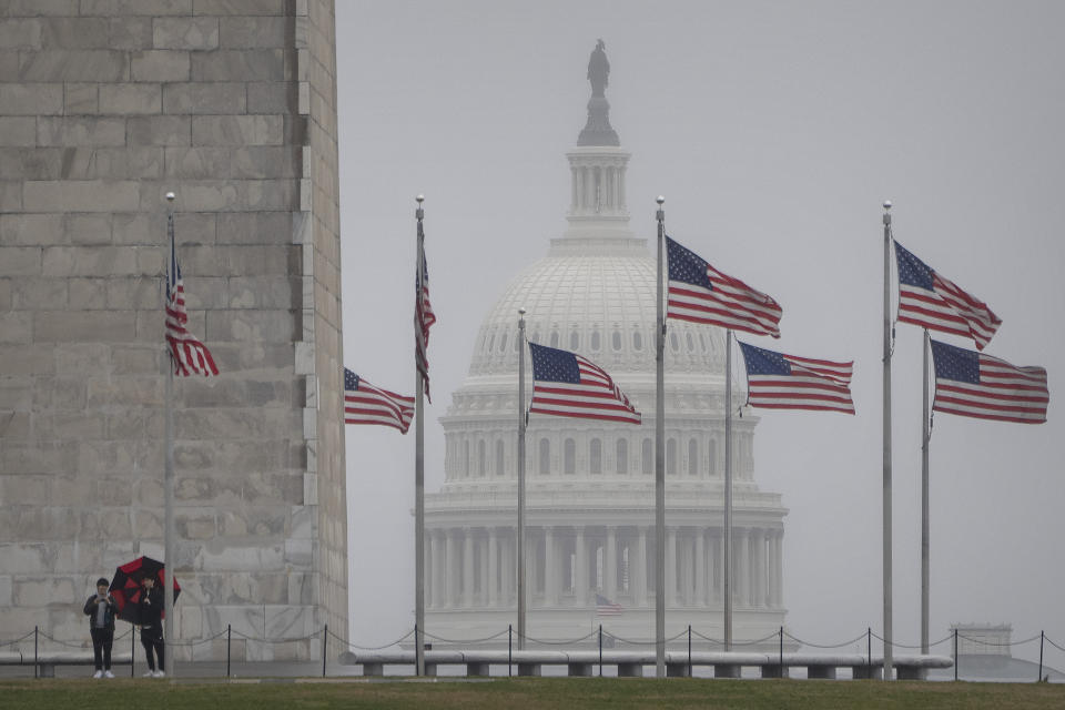 Visitors stand at the base of the Washington Monument as the dome of the Capitol is seen in the distance on a rainy morning, Tuesday, March 5, 2024, in Washington. President Joe Biden and former President Donald Trump are poised to move much closer to winning their party's nominations during the biggest day of the primary campaign on Tuesday, setting up a historic rematch that many voters would rather not endure. (AP Photo/Mark Schiefelbein)