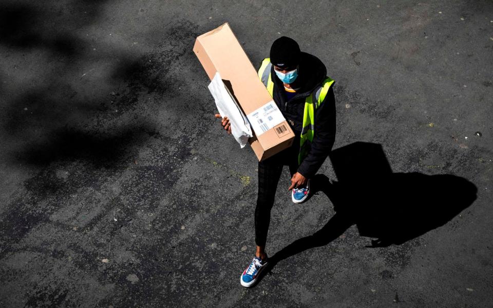 A delivery man wearing a protective mask carries an Amazon box and a letter in a street of Paris on April 15, 2020 on the 30th day of a lockdown in France aimed at curbing the spread of the COVID-19 infection caused by the novel coronavirus - Joel Saget/AFP/Getty