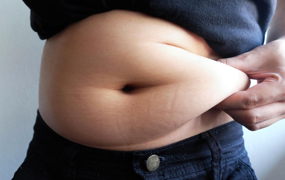 Midsection Of Overweight Woman Holding Stomach Fats While Standing Against Wall