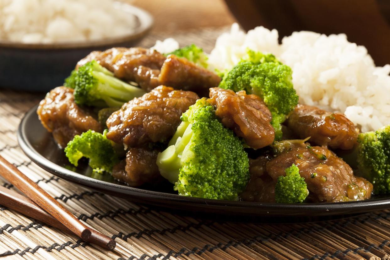 Beef and Broccoli on black plate on bamboo mat with chopsticks