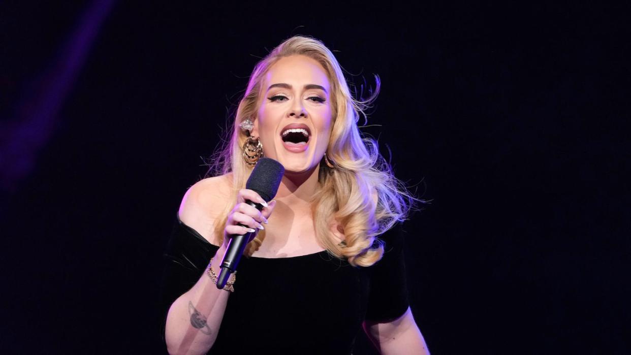 adele holding a microphone in her right hand and leaning forward as she is singing