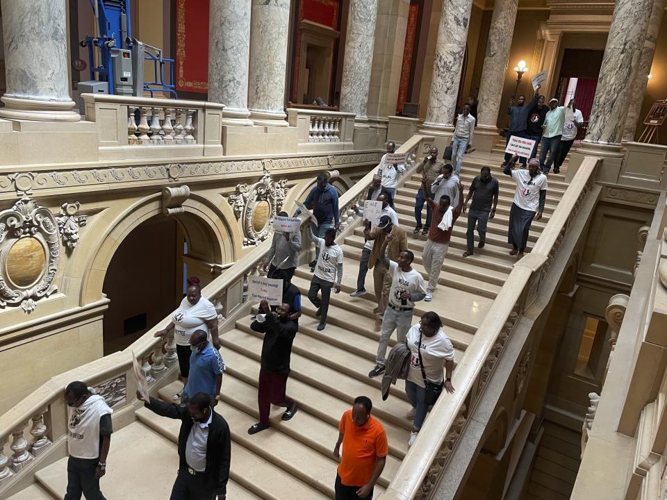 Dozens of protesters descend a staircase in the Minnesota State Capitol building in St. Paul, Minn., Friday, May 17, 2024, while holding signs and pushing for a law that would require ride-hailing companies – including Uber and Lyft -- to increase pay for drivers in the state. Uber and Lyft have said they will leave the state if Minnesota lawmakers pass legislation requiring the companies to raise driver pay by more than the companies want to. (AP Photo/Trisha Ahmed)