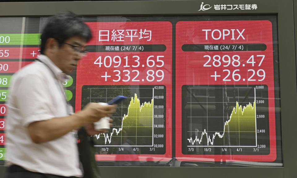 A passerby walks past an electronic stock board showing Japan's Nikkei 225 index, center, at a securities firm Thursday, July 4, 2024 in Tokyo. Japan’s Nikkei 225 benchmark closed Thursday at a fresh record high of 40,913.65, pushing past its most recent record close set in March. (Kyodo News via AP)