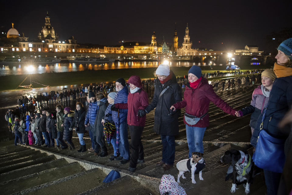 People form a human chain on the banks of the Elbe river with the historical old town in background, marking the 75th anniversary of the destruction of Dresden in the Second World War, in Dresden, Germany, Thursday Feb. 13, 2020. A 1945 allied bombing campaign reduced the centre of Dresden to rubble leaving about 25,000 people dead. (Robert Michael/dpa via AP)