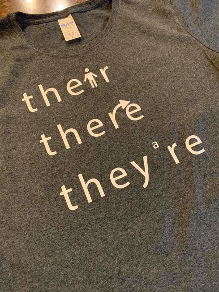 a t shirt that says their with a person in the i, there with the r incorporating an arrow, and theyre with an a where the apostrophe would be