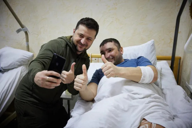 In this handout picture released and taken by Ukrainian Presidency Press Office on March 13, 2022, Ukrainian President Volodymyr Zelensky (L) snaps a selfie with an injured man laying on a bed during a visit at a military hospital following fightings in the Kyiv region (UKRAINIAN PRESIDENTIAL PRESS SER)