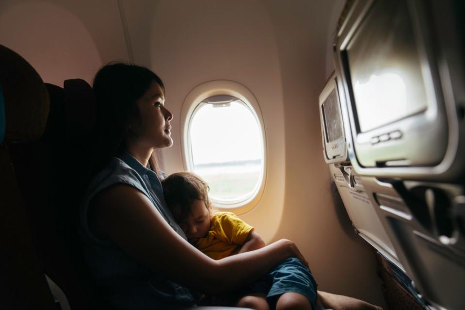 Baby sleeps in mom’s arms while on an airplane in flight via Getty Images