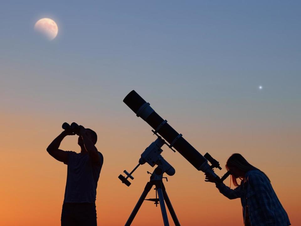 Couple stargazing together with a astronomical telescope, looking at planets, stars, lunar eclipse and meteor shower.