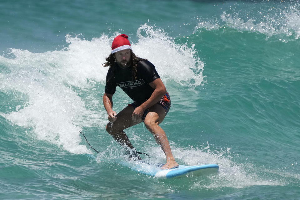 Tony O'Connor, originally from Manchester, England, rides a surfboard while wearing a Santa hat as he celebrates Christmas at Bondi Beach in Sydney, Saturday, Dec. 25, 2021. (AP Photo/Rick Rycroft)