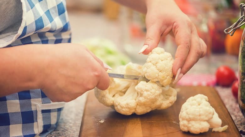 Person cutting cauliflower on board