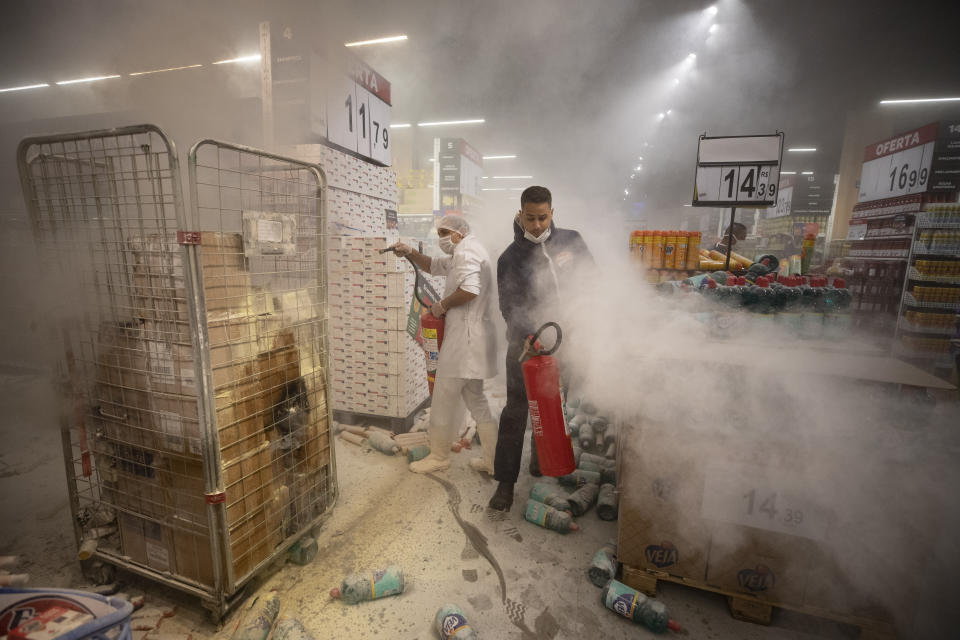 Employees douse a fire set by protesters inside a Carrefour supermarket during a protest against the murder of Black man Joao Alberto Silveira Freitas at a different Carrefour supermarket the night before, on Brazil's National Black Consciousness Day in Sao Paulo, Brazil, Friday, Nov. 20, 2020. Freitas died after being beaten by supermarket security guards in the southern Brazilian city of Porto Alegre, sparking outrage as videos of the incident circulated on social media. (AP Photo/Andre Penner)