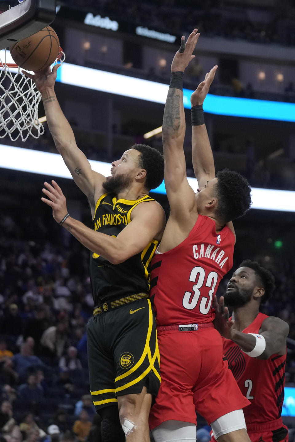 Golden State Warriors guard Stephen Curry, left, scores past Portland Trail Blazers forward Toumani Camara (33) and center Deandre Ayton during the second half of an NBA basketball game in San Francisco, Saturday, Dec. 23, 2023. (AP Photo/Jeff Chiu)