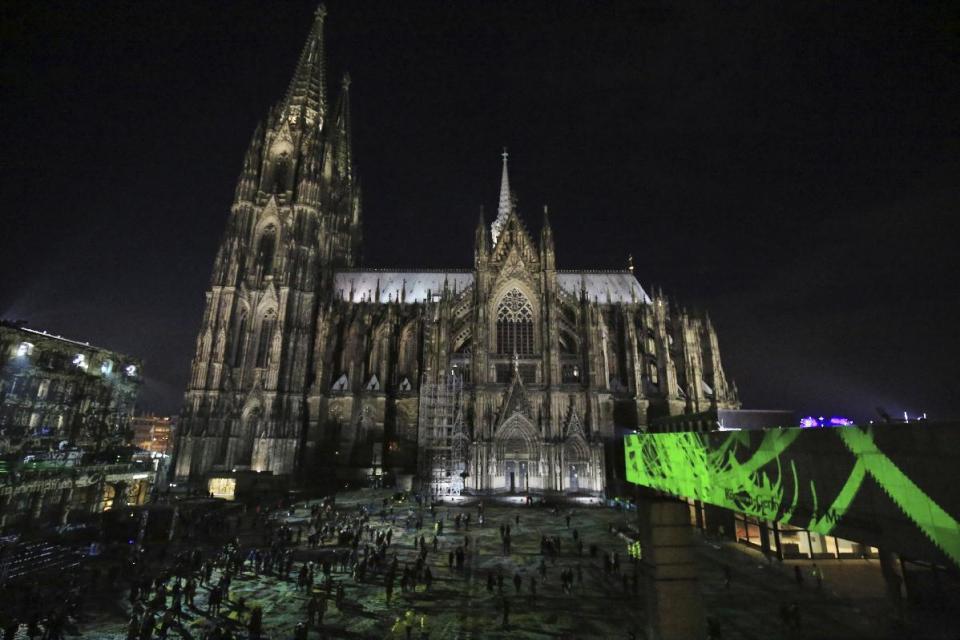 Tourists walk through the light installation by Berlin artist Phillip Geist in front of the Cologne cathedral, Saturday, Dec. 31, 2016 where a string of robberies and sexual assaults last year that were blamed largely on migrants from North Africa prompted nationwide outrage. (Oliver Berg/dpa via AP)