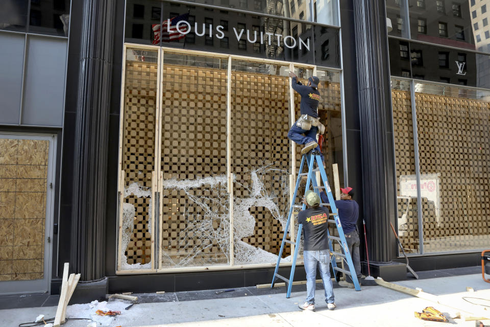 Trabajadores cubren con tablones un escaparate de una tienda de la cadena Louis Vuitton el lunes 10 de agosto de 2020, después de los saqueos registrados en negocios del centro de Chicago. (AP Foto/Teresa Crawford)