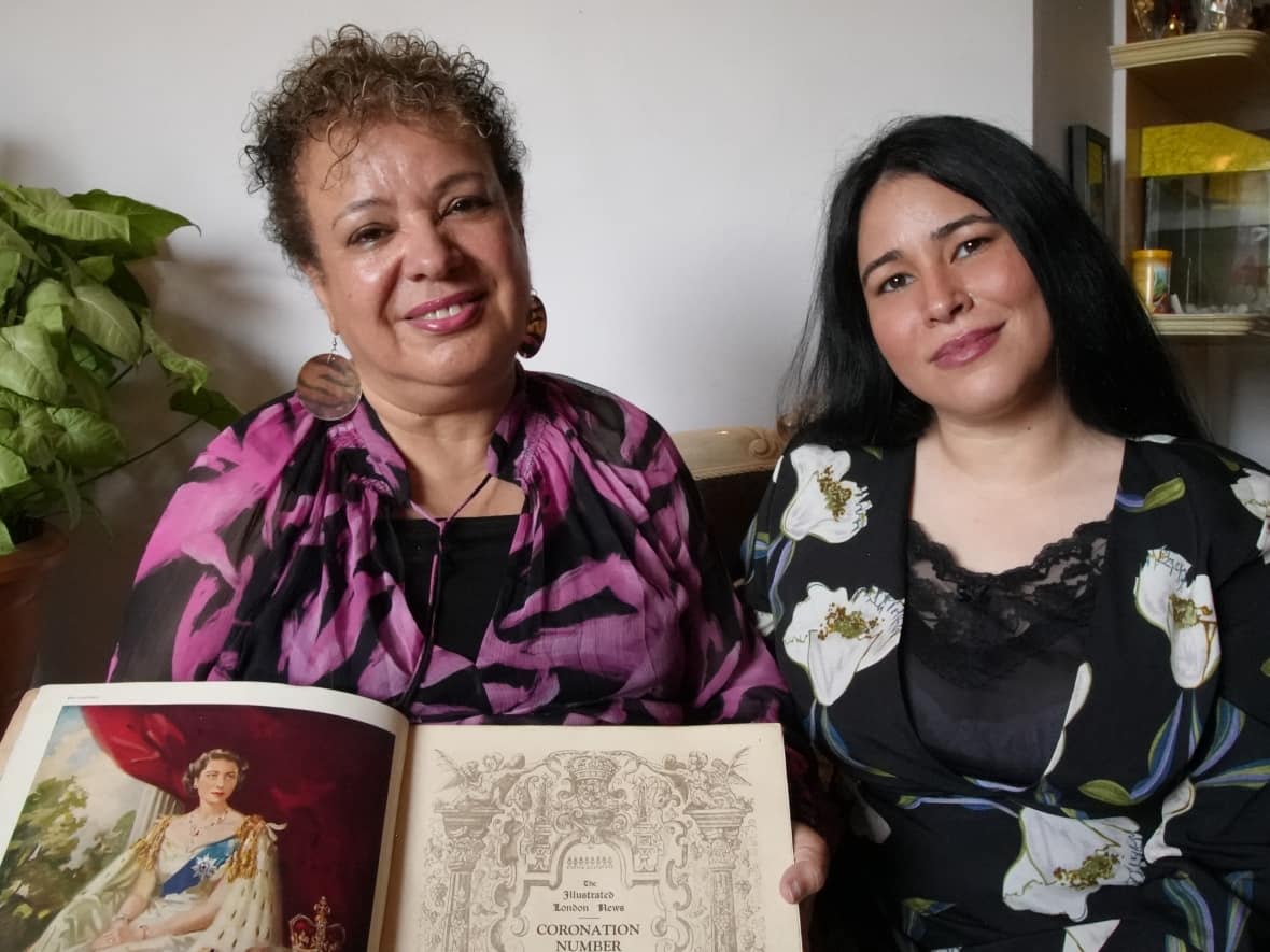 Sarvar Irani, 62, sits with her daughter Sharon holding one of the many books in her collection of memorabilia. She's been accumulating souvenirs of the British royal family for decades.  (Salimah Shivji/CBC - image credit)