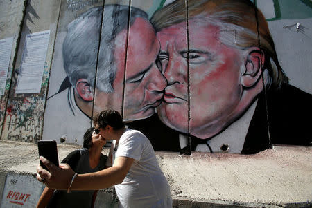 Tourists kiss each other as they stand in front of a mural depicting U.S. President Donald Trump and Israel's Prime Minister Benjamin Netanyahu kissing each other in the West Bank city of Bethlehem October 29, 2017. REUTERS/Mussa Qawasma