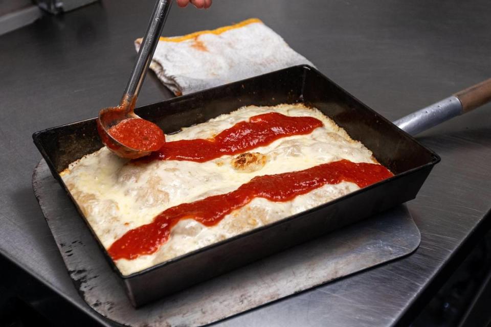 Matty Evans, chef of Rise Up! Pizza, applies tomato sauce on the top of the melted cheese on a Detroit-style pizza.