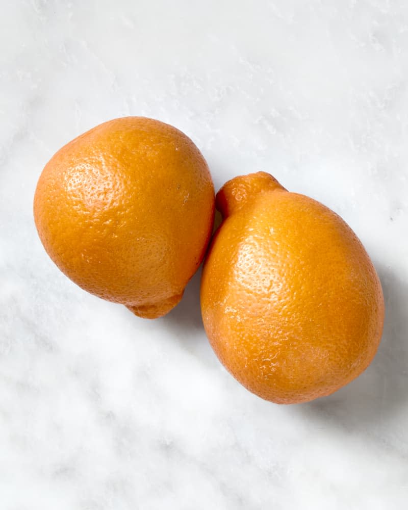 overhead shot of two tangelos on a white marble surface.