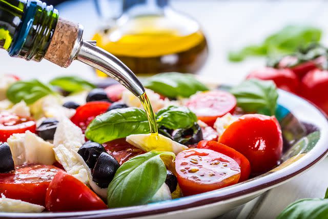 <p>Getty Images</p> Olive oil being poured into a Caprese salad