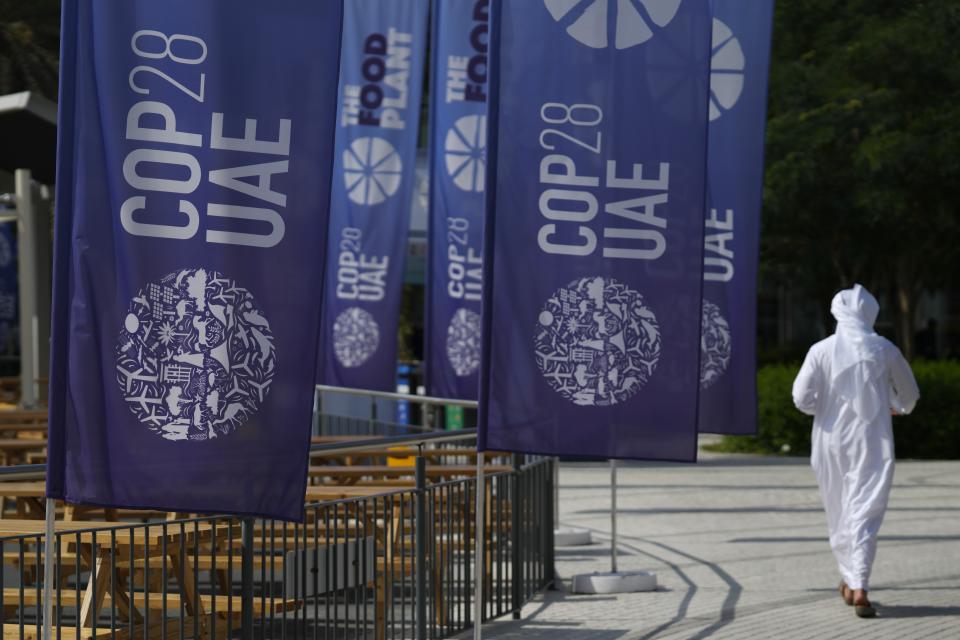 A person walks near signs for the COP28 U.N. Climate Summit, Tuesday, Nov. 28, 2023, in Dubai, United Arab Emirates. (AP Photo/Peter Dejong)