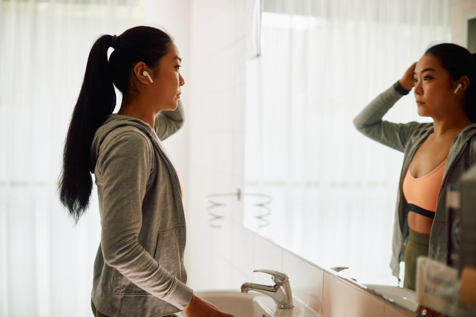 Young Asian sportswoman standing in front of a mirror in public bathroom at the gym.